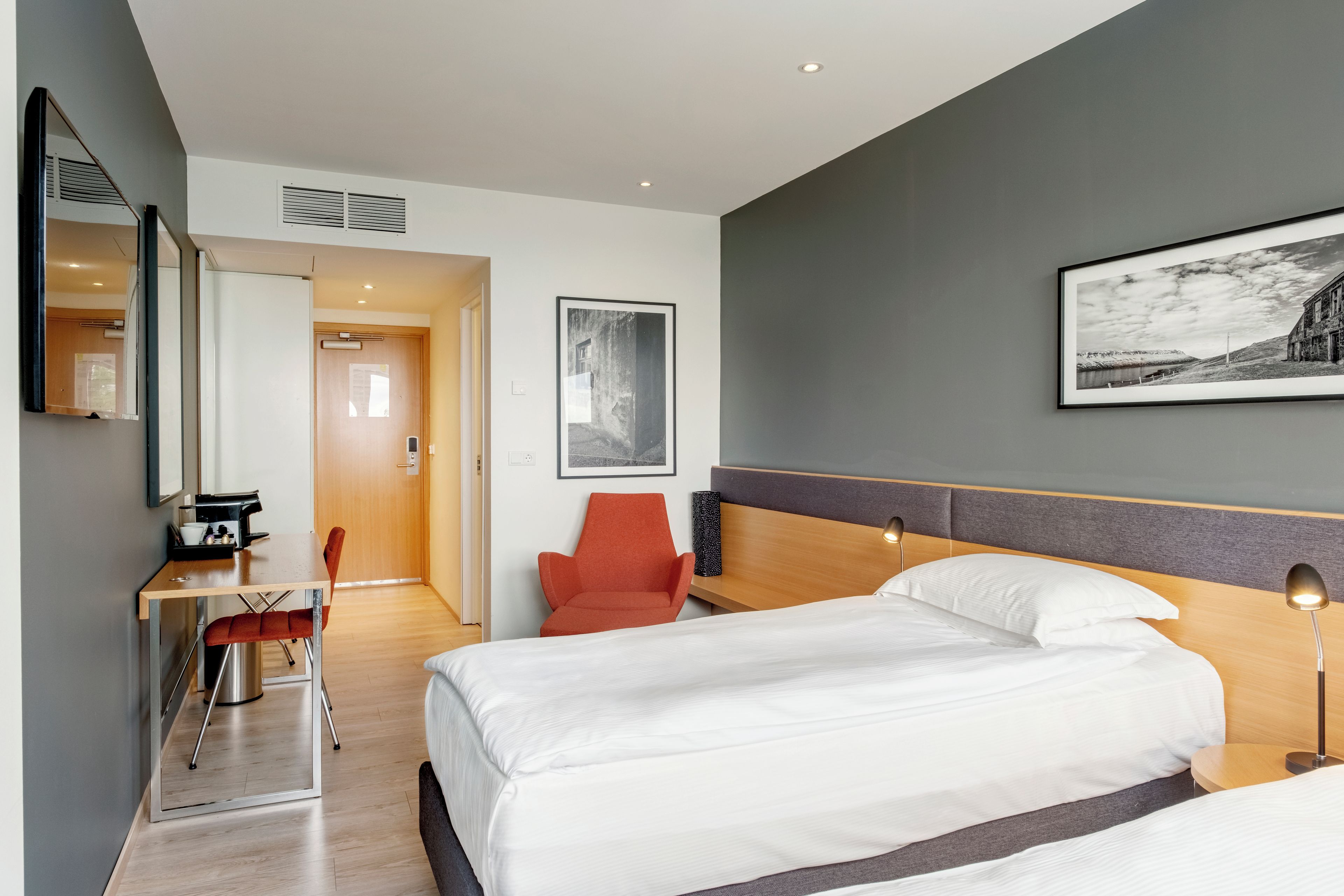 A hotel room with a bed, a desk, a chair, and a large framed picture on the wall.