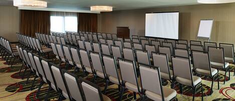 A conference room with rows of chairs, a projector screen, and a whiteboard.
