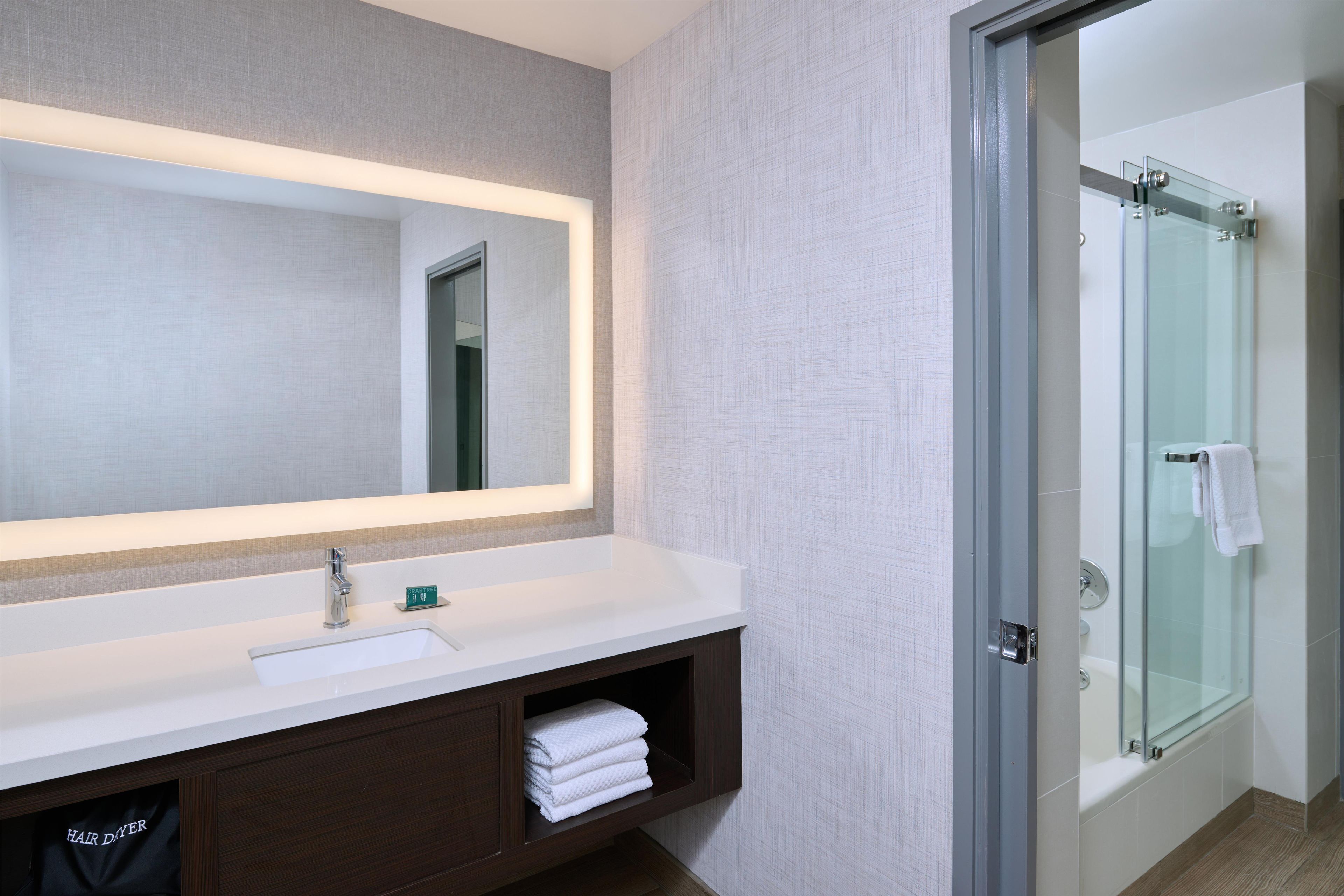 A modern bathroom with a large mirror, a sink, and a glass shower enclosure.
