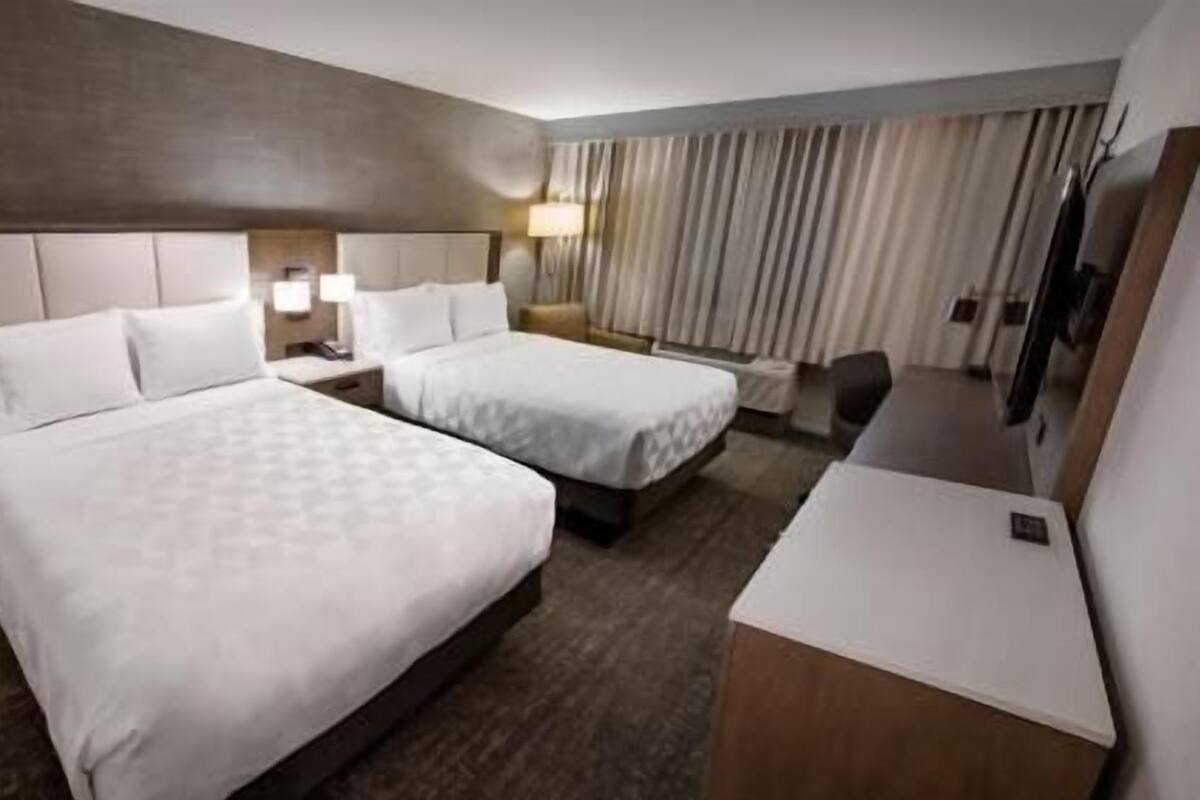 Habitación de hotel con dos camas, un escritorio, una silla, un televisor y una ventana con cortinas.