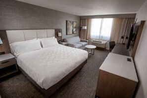 Habitación de hotel con una cama grande, un sofá, un escritorio, un televisor y una ventana con cortinas.