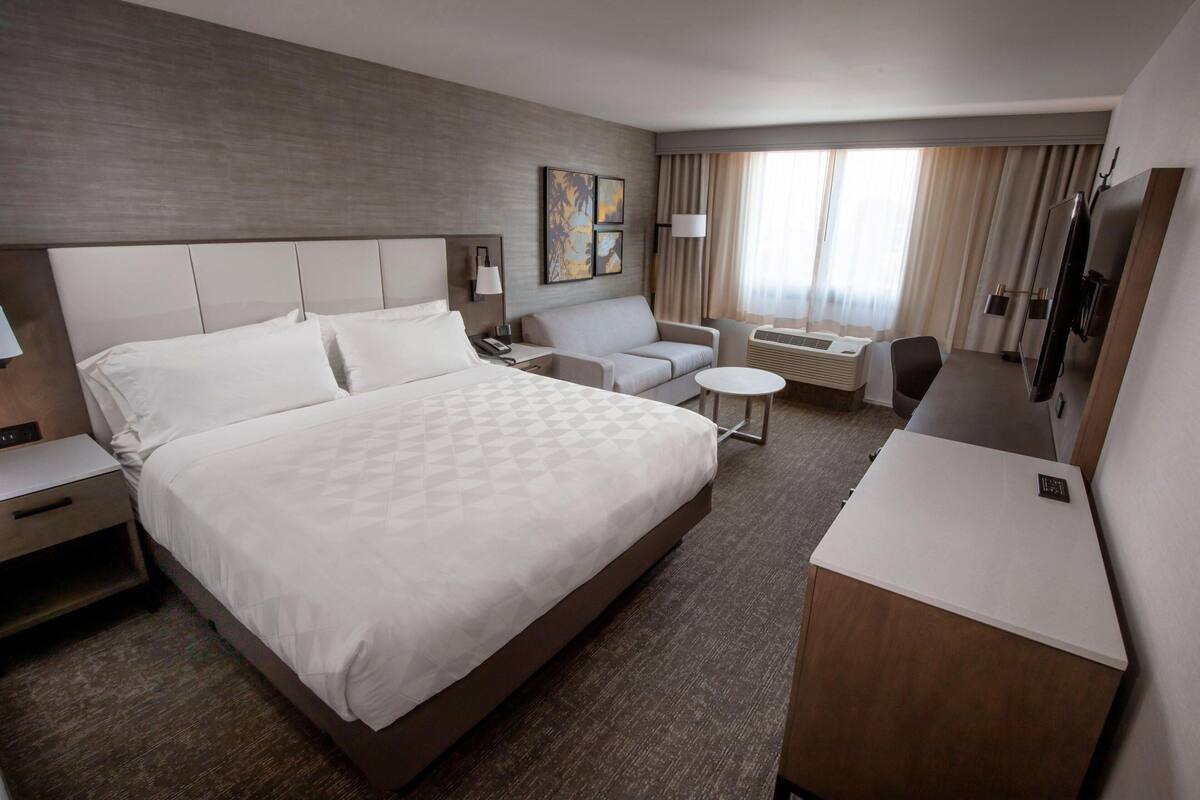 Habitación de hotel con una cama grande, un sofá, un escritorio, un televisor y una ventana con cortinas.