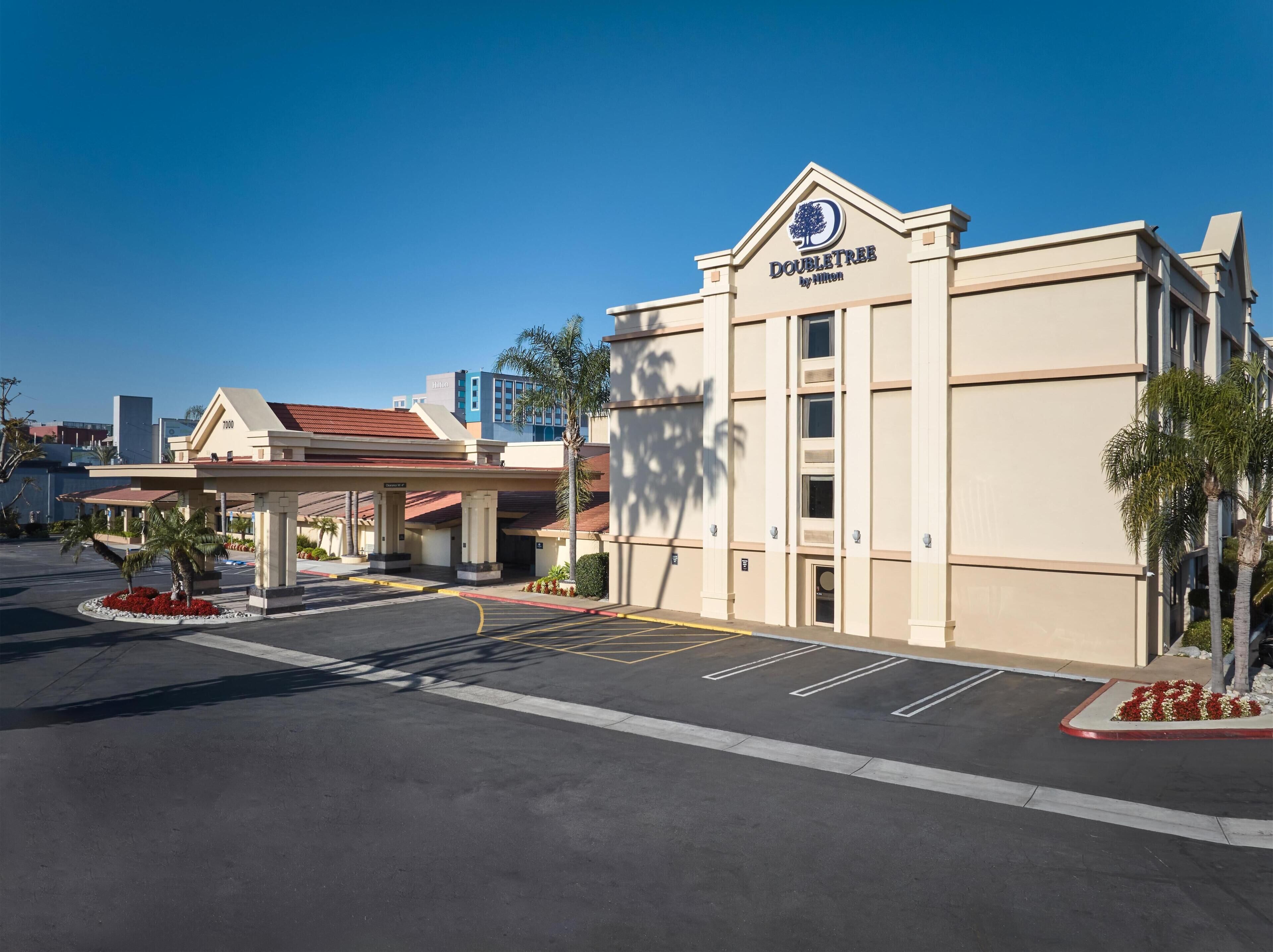 A DoubleTree by Hilton hotel with a parking lot, palm trees, and a clear blue sky.