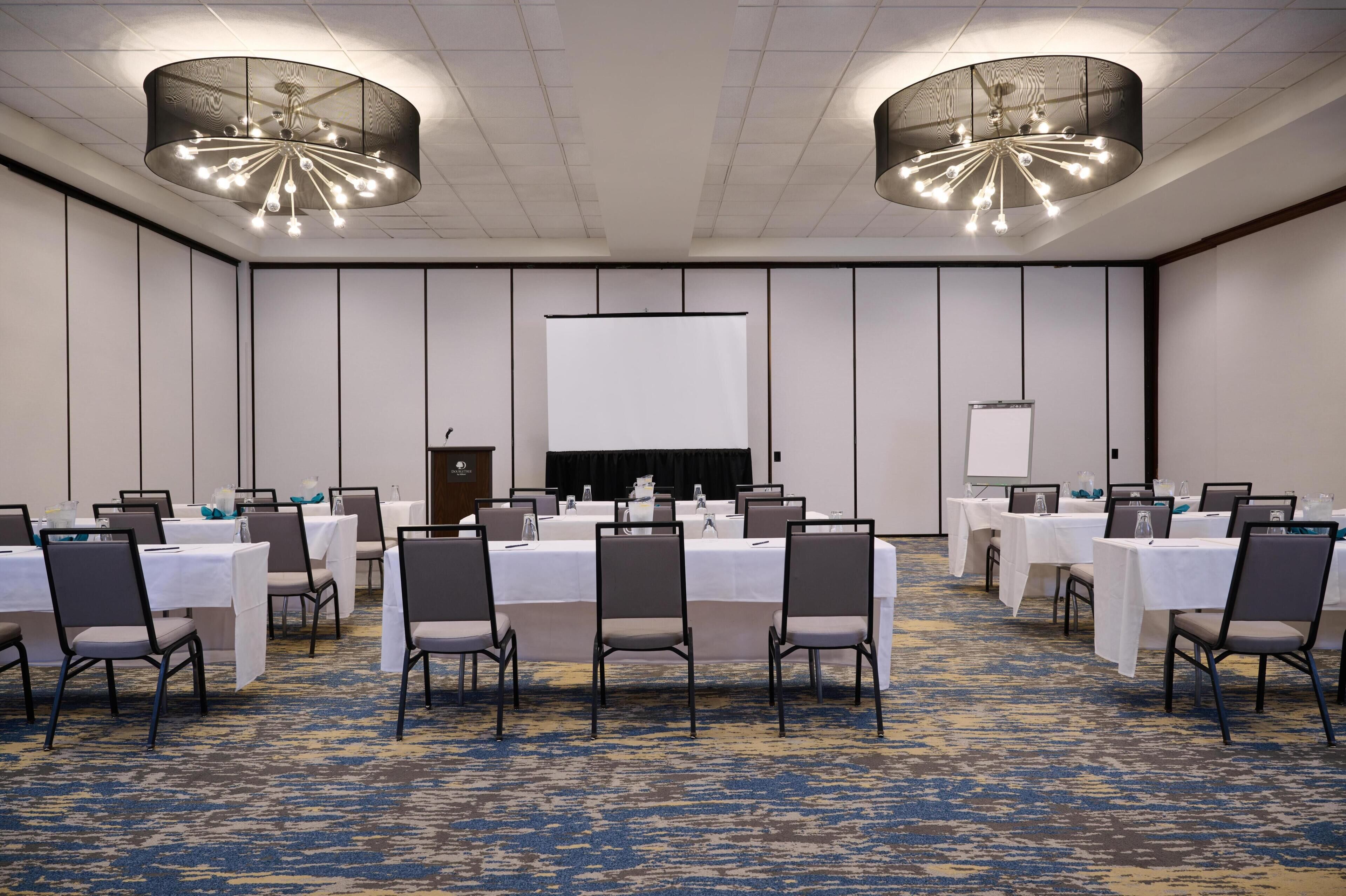 A conference room with tables, chairs, a projector screen, and a carpeted floor.