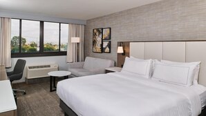Habitación de hotel con una cama grande, un escritorio, una silla, una mesita y una ventana con cortinas.