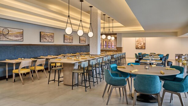 Un comedor moderno con largas mesas comunes, sillas individuales y lámparas colgantes.