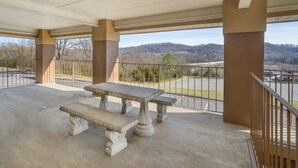 An outdoor patio with a stone table and benches, overlooking a parking area and hilly landscape.