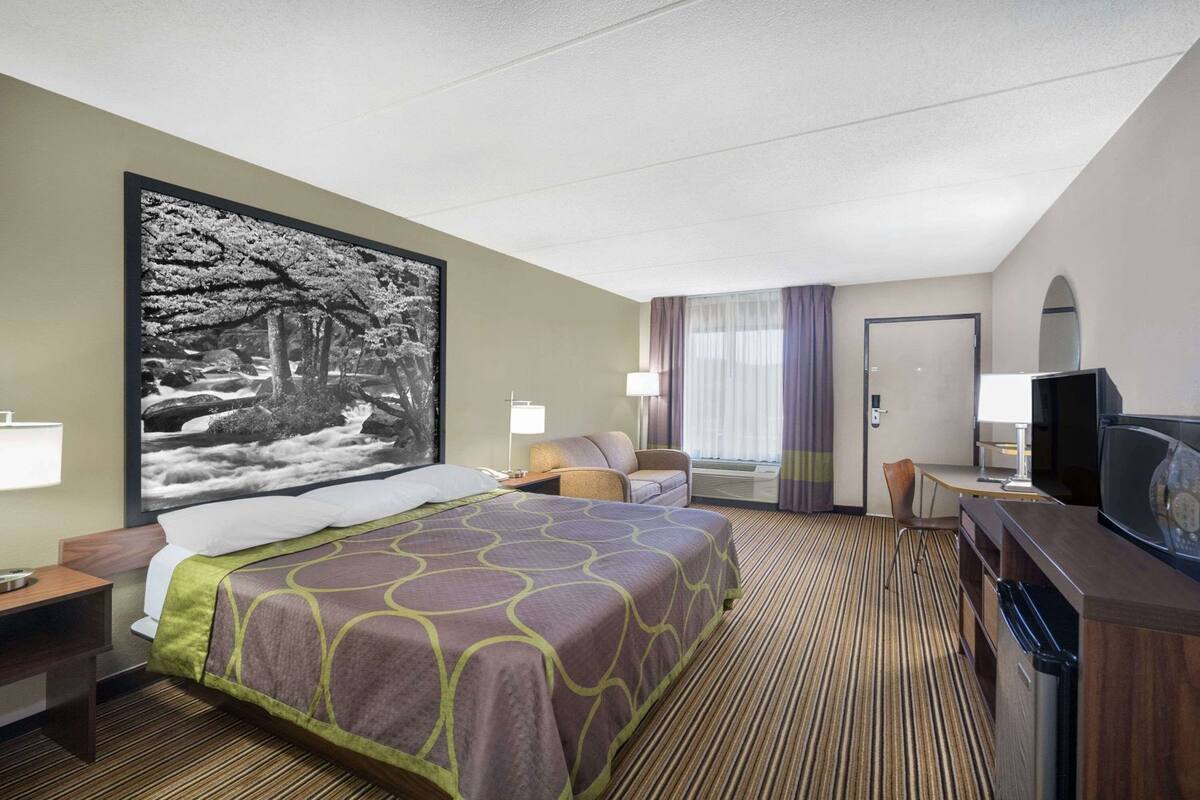Une chambre d’hôtel avec un grand lit, un bureau avec une chaise, une télévision et une grande fenêtre avec des rideaux.