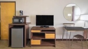 A hotel room with a bed, a desk with a chair, a television, a small refrigerator, and a microwave.