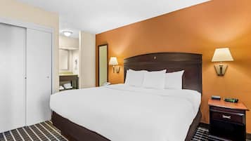 A hotel room with a bed, bedside lamps, a nightstand, and a bathroom visible through an open door.