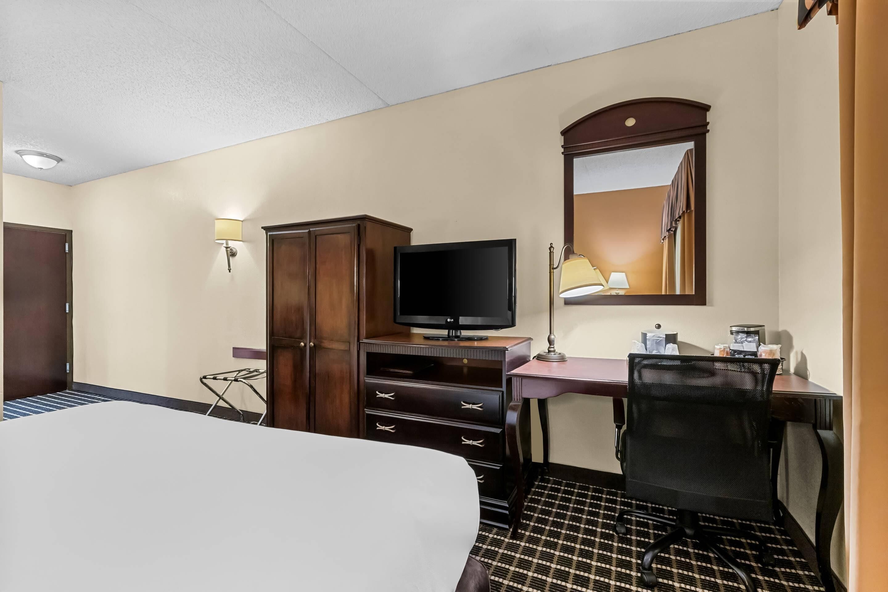 Une chambre d’hôtel équipée d’un lit, d’une télévision, d’un bureau avec une chaise, d’une armoire et d’un miroir.