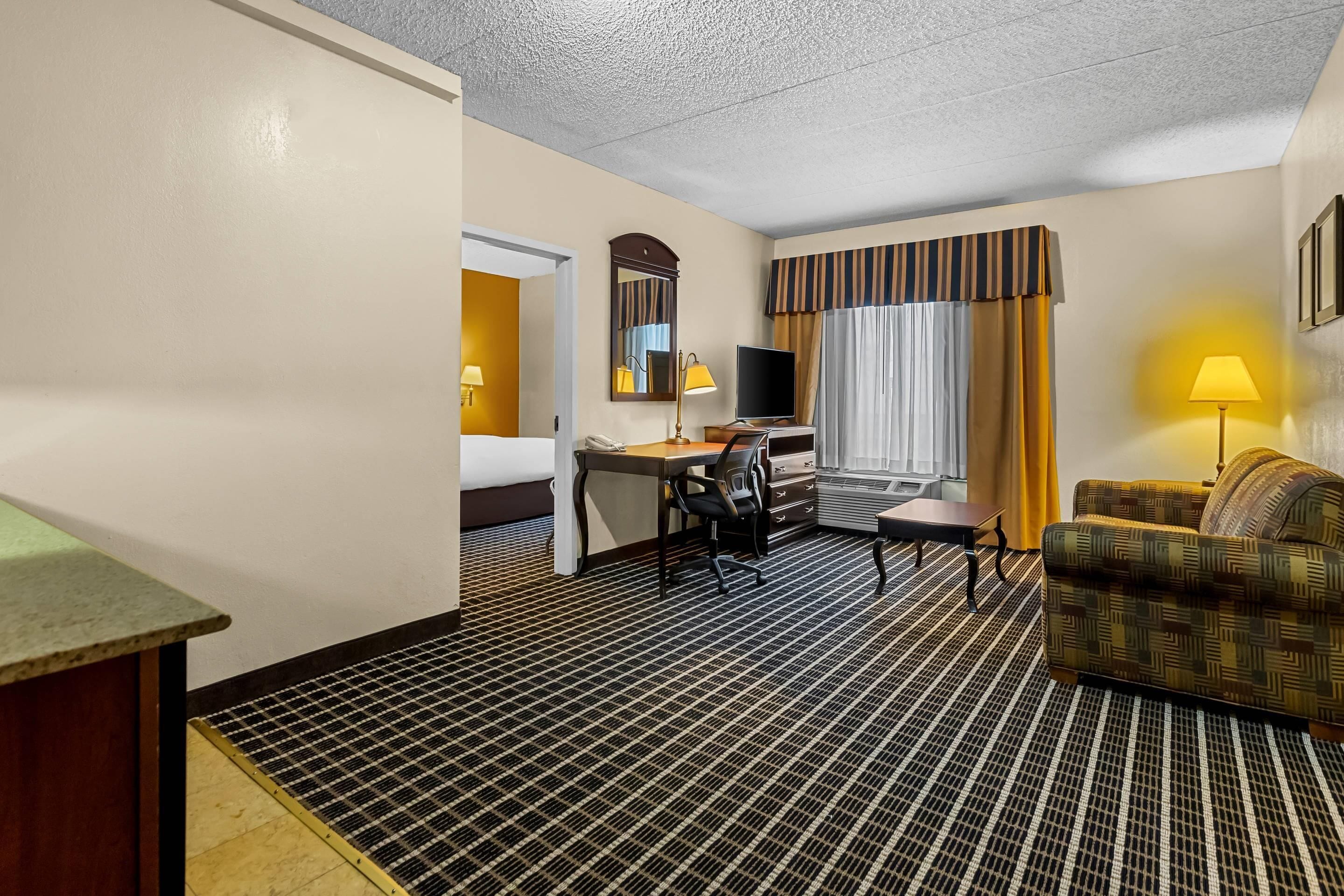 Une chambre d’hôtel comprenant un lit, un bureau avec une chaise, une télévision, un canapé et une fenêtre avec des rideaux.