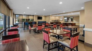 A modern restaurant with multiple tables and chairs, a kitchen area, and a TV mounted on the wall. - Comfort Inn & Suites Somerset - New Brunswick (Somerset)