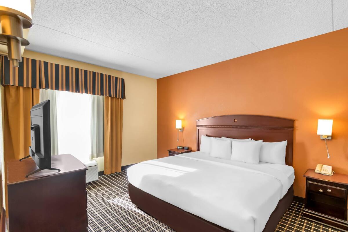 A hotel room with a large bed, a desk with a computer, two bedside lamps, and a window with curtains.