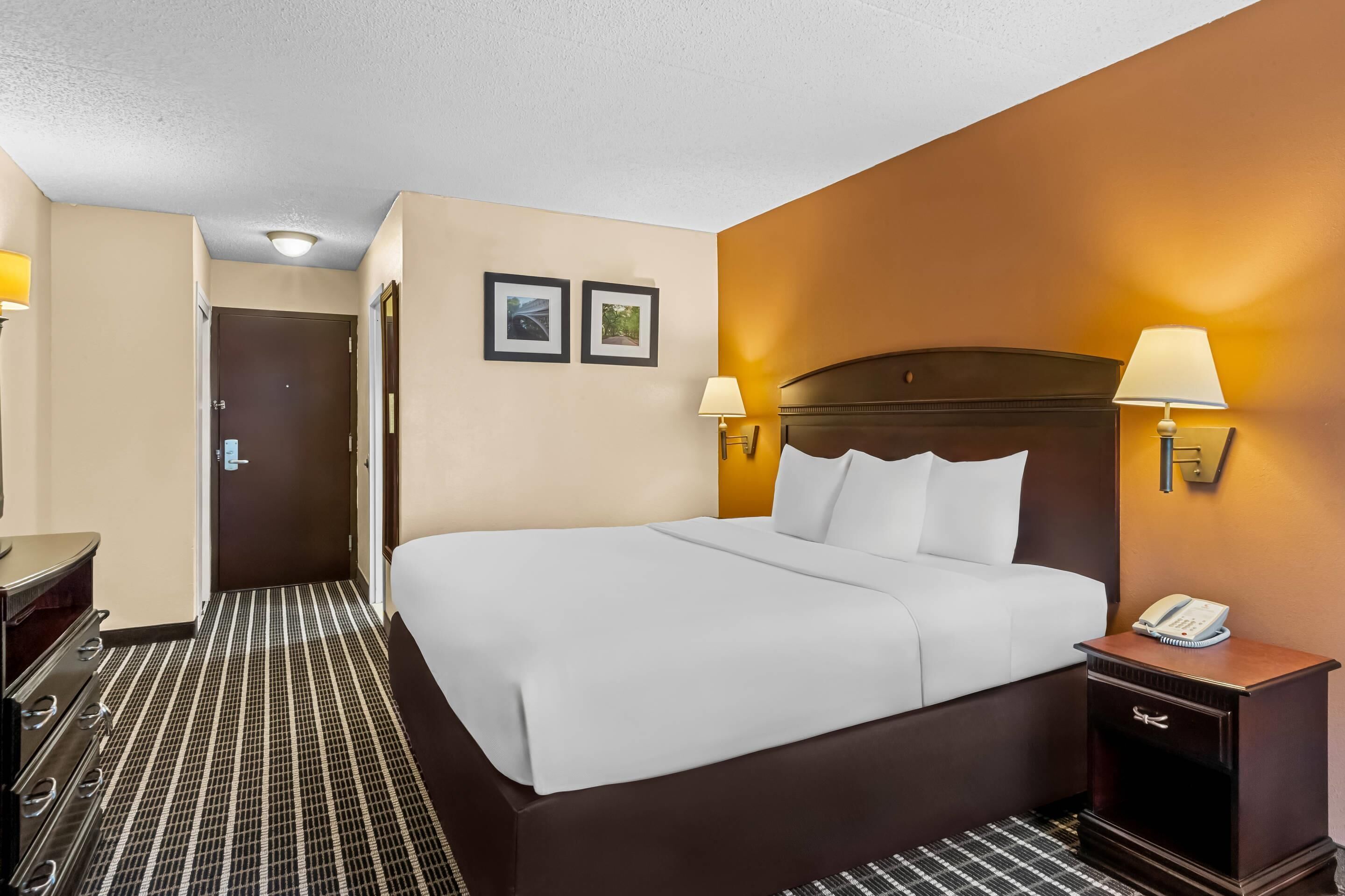 A hotel room with a large bed, bedside lamps, a phone, and a door leading to a hallway.