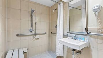 A bathroom with a shower, a sink, a mirror, and a hairdryer.