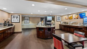 A hotel lobby with a reception desk, a coffee station, and a seating area with tables and chairs.
