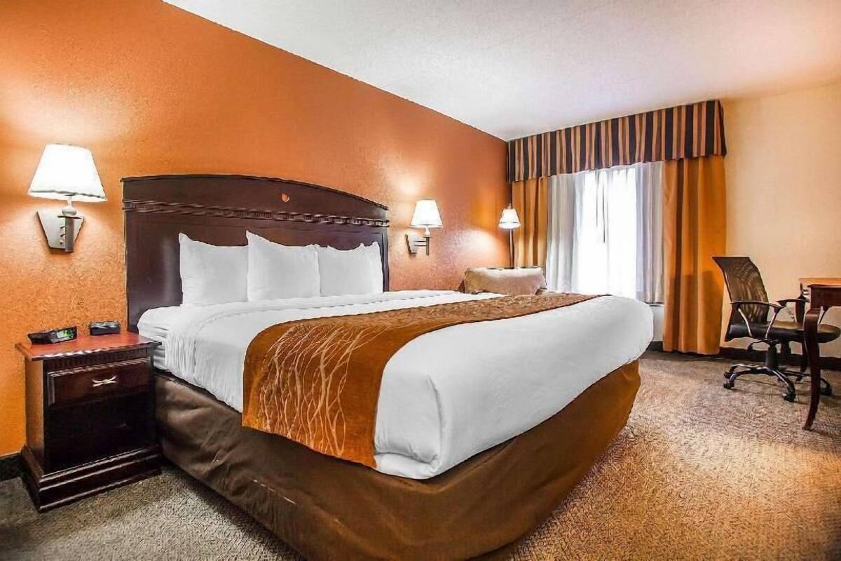A hotel room with a large bed, two bedside tables with lamps, a desk with a chair, and a window with curtains.