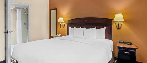 Habitación de hotel con una cama grande, dos lámparas de noche, una mesita de noche con un reloj y una puerta que da a un baño.