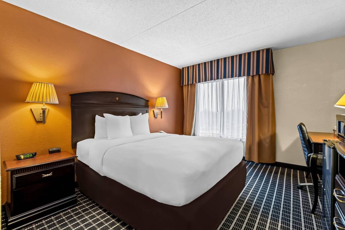 A hotel room with a bed, bedside lamps, a desk, and a chair.