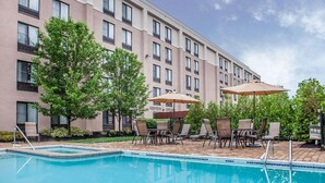 A swimming pool with lounge chairs and umbrellas, surrounded by a building with multiple windows and balconies.