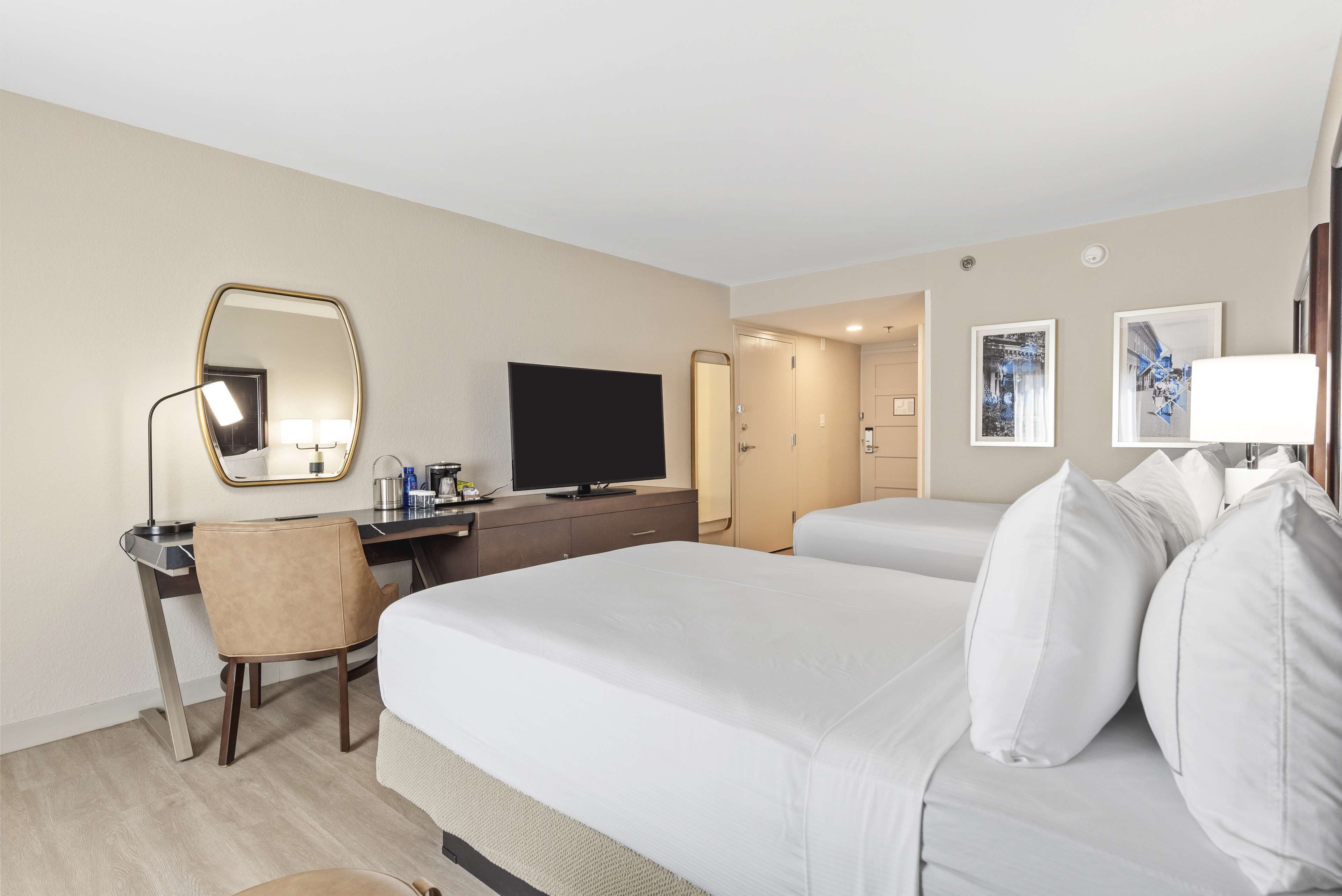 A hotel room with a bed, a desk, a chair, a television, a mirror, and a door leading to a bathroom.