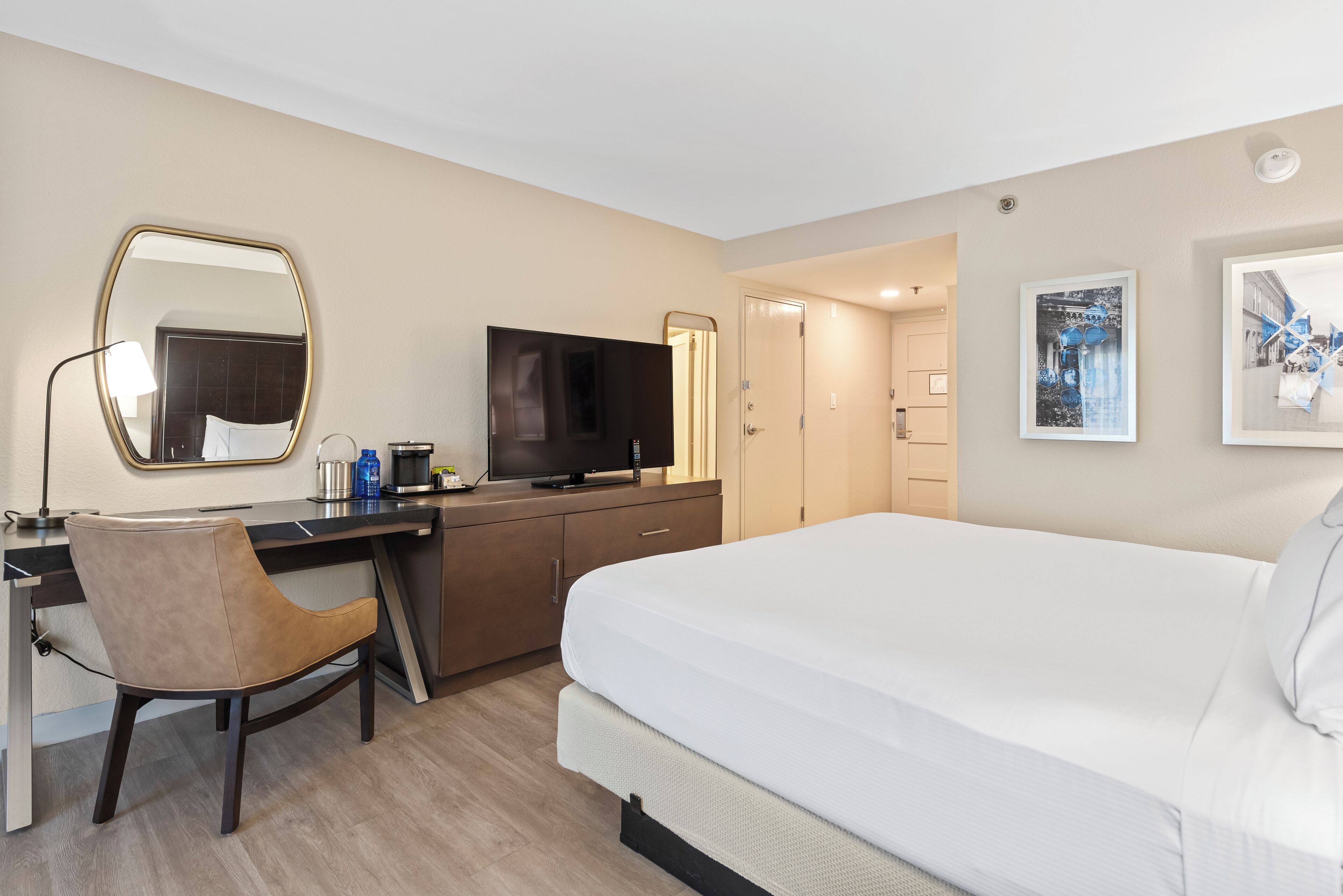 A hotel room with a bed, desk, chair, TV, and artwork on the walls.