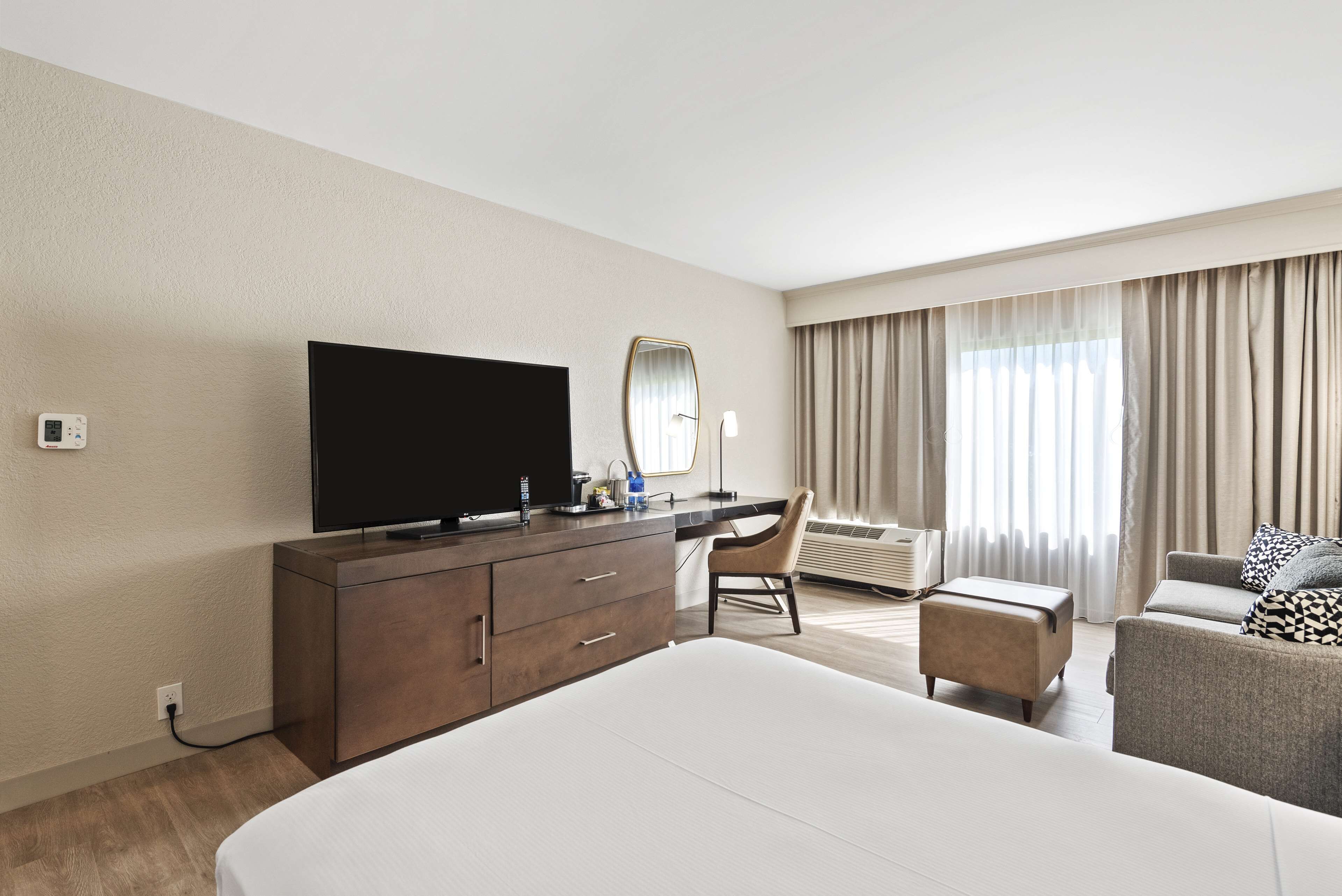 Ein Hotelzimmer mit einem großen Bett, einem Schreibtisch mit Flachbildfernseher, einem Sessel, einem kleinen Hocker und einem Sofa.