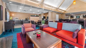 A hotel lobby with a seating area, a kitchen in the background, and a television screen. - MainStay Suites Appleton Airport - Fox River Mall Area (Appleton)
