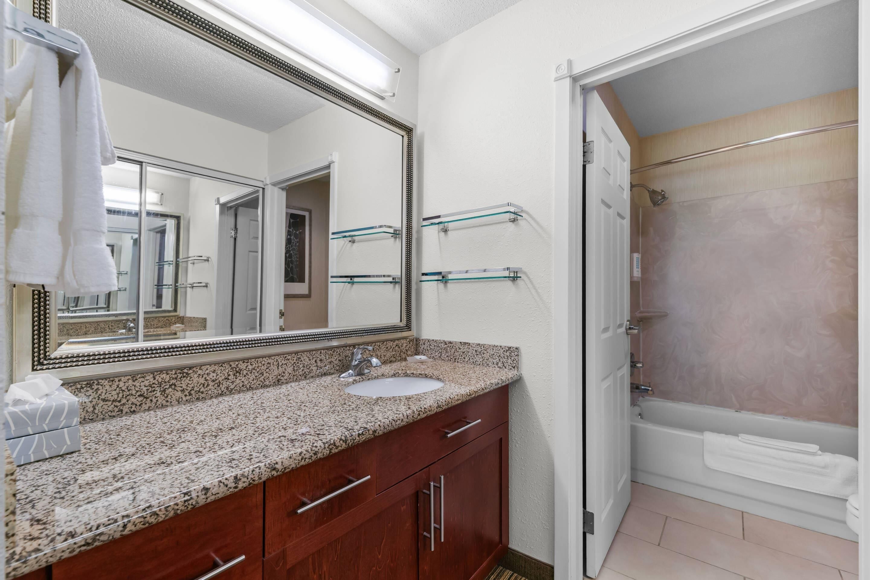 A bathroom with a granite countertop sink, a large mirror, a glass shower enclosure, and a white bathtub.