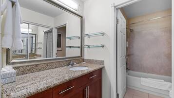 A bathroom with a granite countertop sink, a large mirror, a glass shower enclosure, and a white bathtub.
