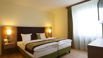 A hotel room with a large bed, nightstands, a desk, and a window with curtains.