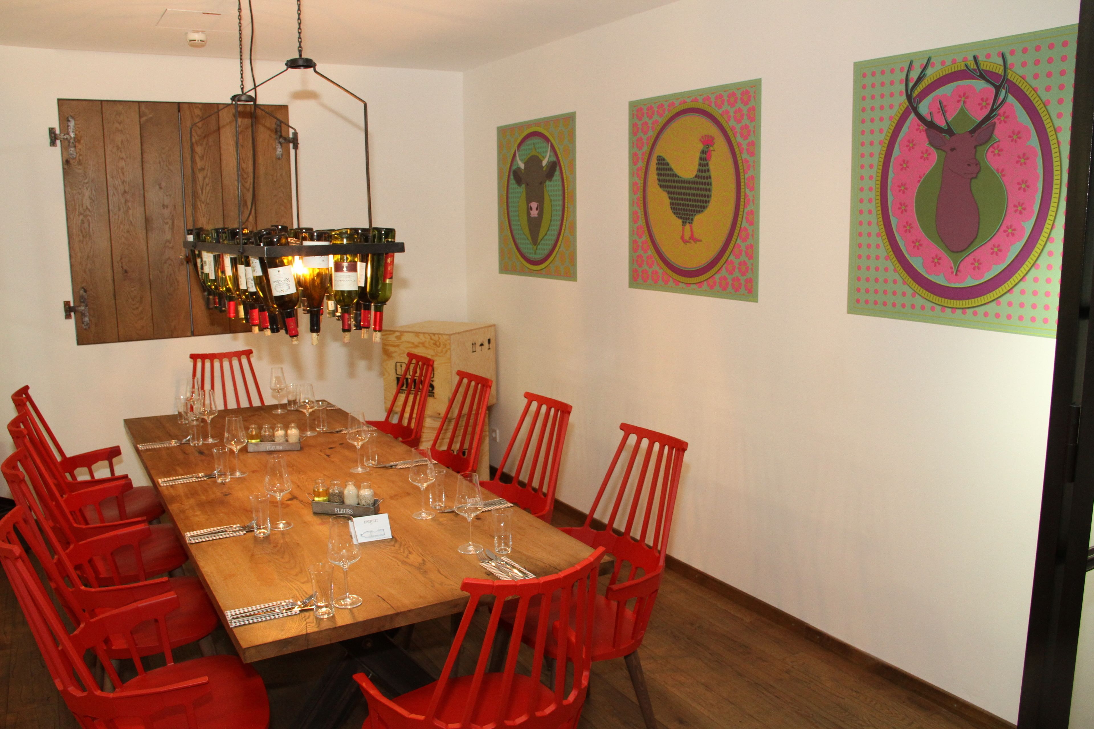 Comedor con una mesa de madera dispuesta para seis personas, rodeada de sillas rojas y decorada con coloridas obras de arte en las paredes.