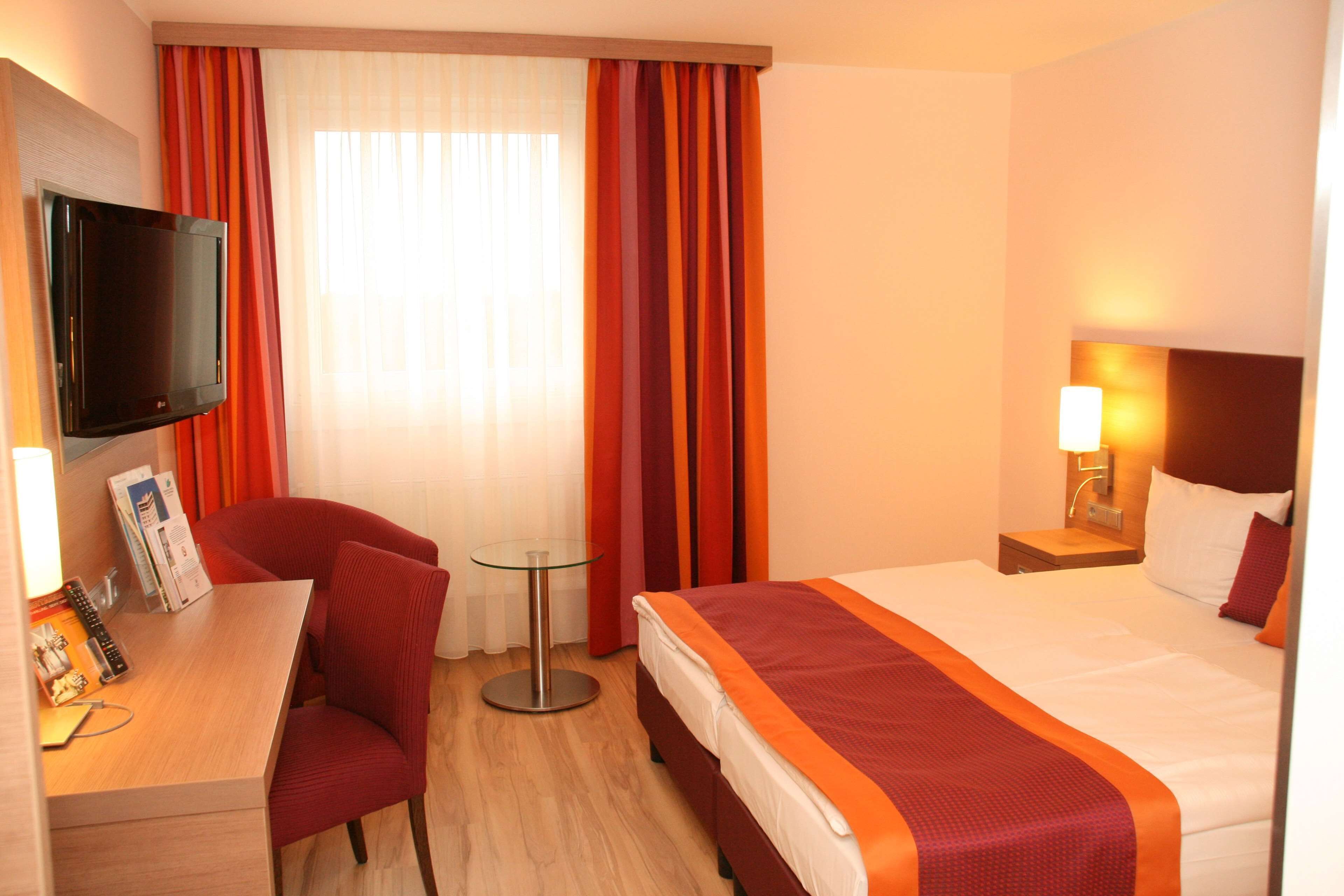 Una camera d'albergo con un letto, una scrivania con una sedia, una televisione e una finestra con tende.