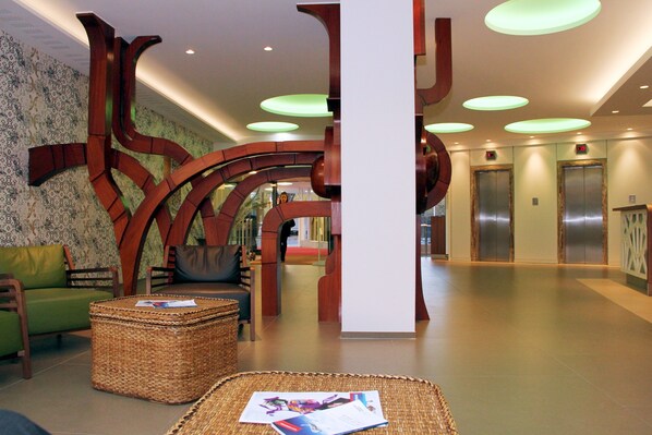 A lobby with a modern design, featuring a green sofa, wicker furniture, and a large abstract sculpture. - Congress Hotel Am Stadtpark (Hannover)