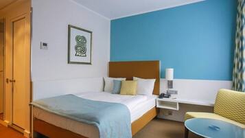 Una habitación de hotel con cama, mesita de noche, silla y una pequeña mesa.