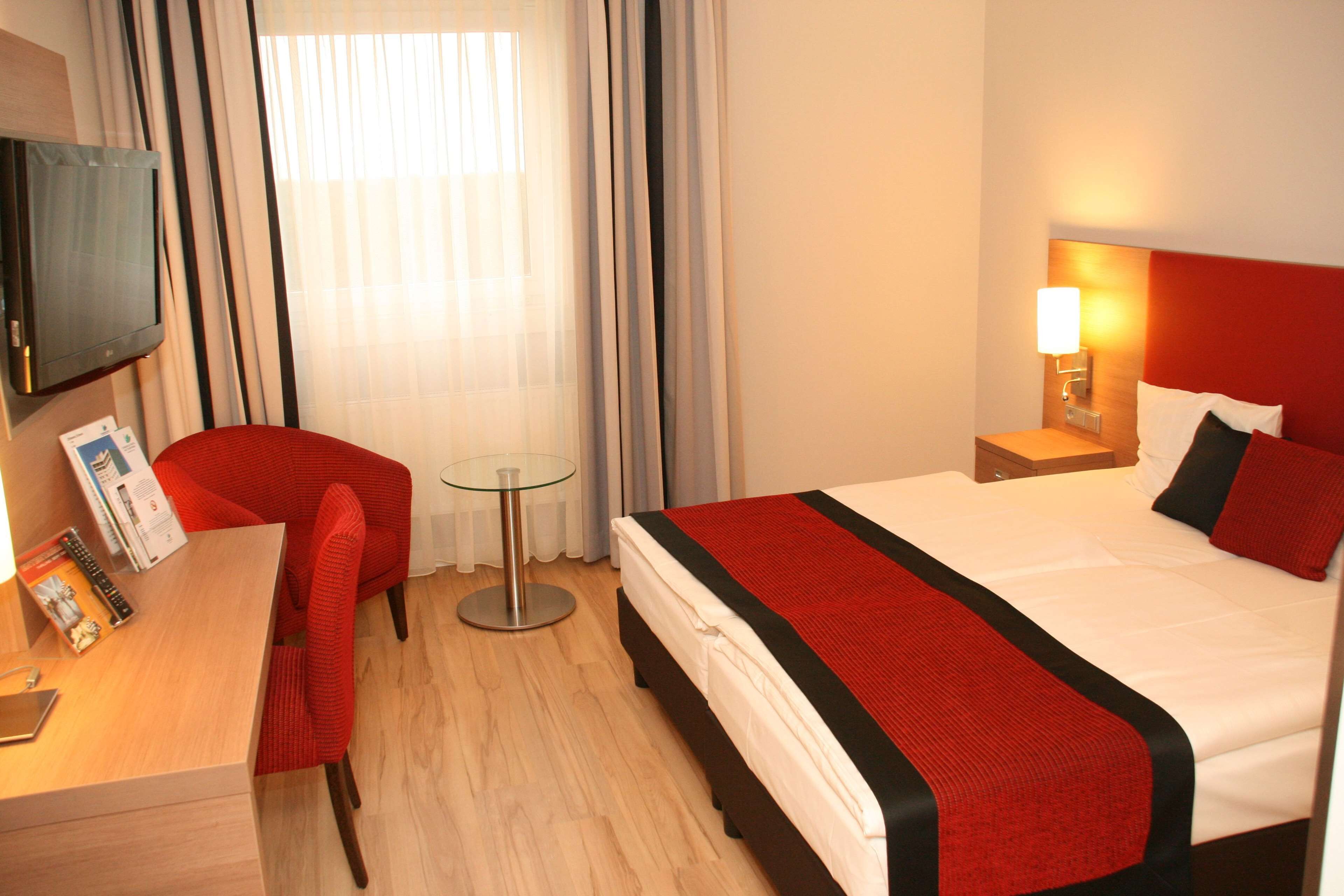 Una habitación de hotel con cama, escritorio, silla, televisor y lámpara.