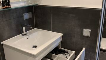 A modern bathroom with a white sink, a mirror, and a storage cabinet.