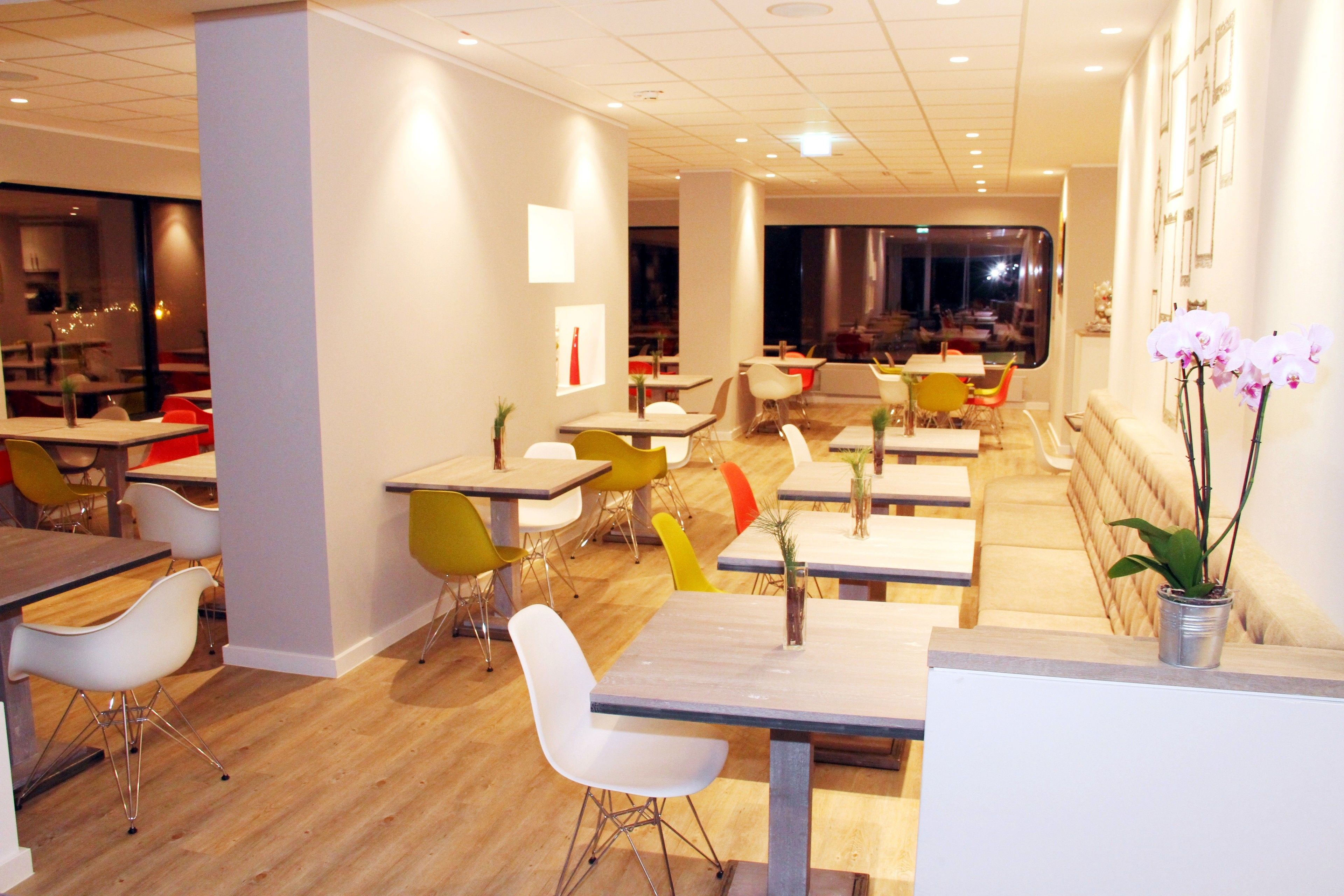 A modern restaurant with multiple dining tables and chairs, a wooden floor, and a view of the dining area through a glass wall.