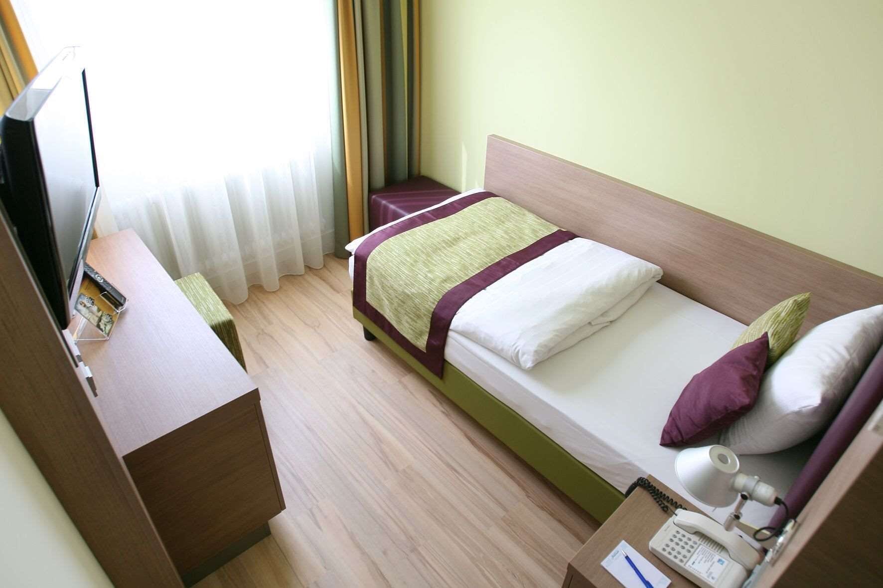 A hotel room with a bed, a desk, a telephone, and a television.