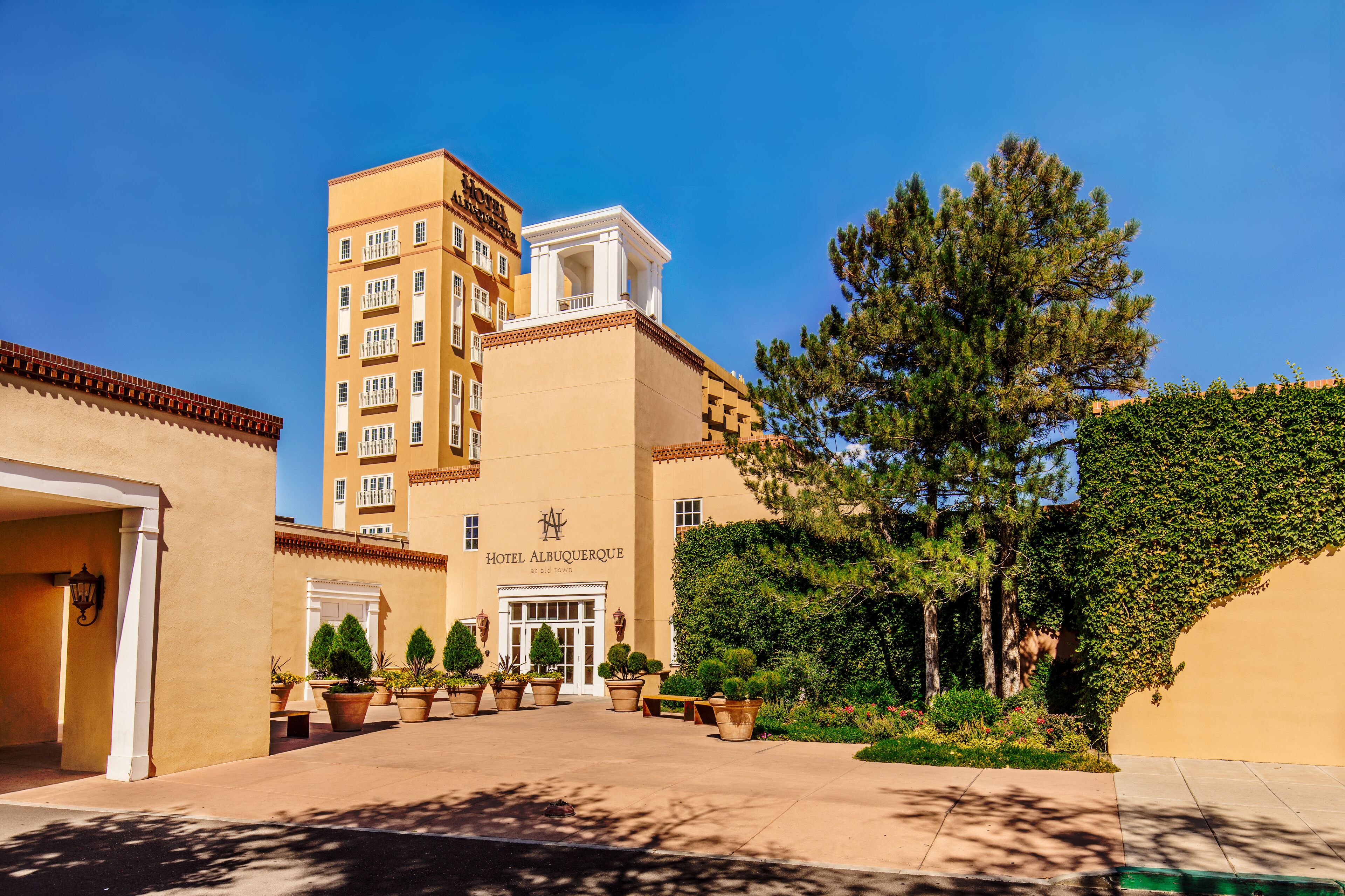 A hotel with a central entrance, multiple floors, and a courtyard with potted plants and trees.