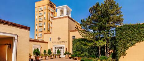 A hotel with a central entrance, multiple floors, and a courtyard with potted plants and trees.