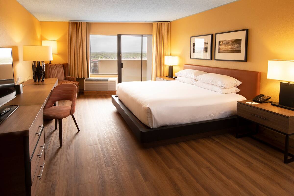 A hotel room with a bed, a desk, a chair, a TV, and a balcony with curtains.