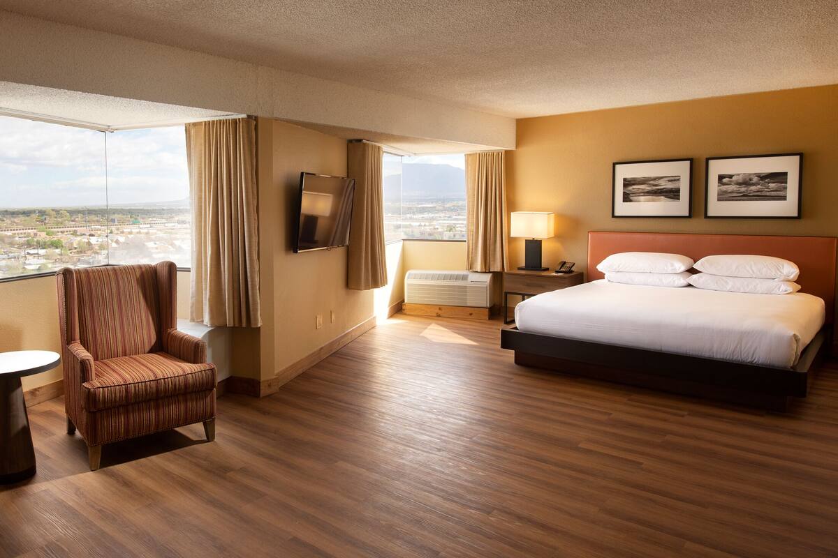 A hotel room with a large bed, a chair, a desk, and a view of a cityscape.