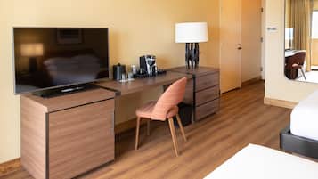 Quarto de hotel com escrivaninha de madeira, televisão, luminária, cadeira e cama.