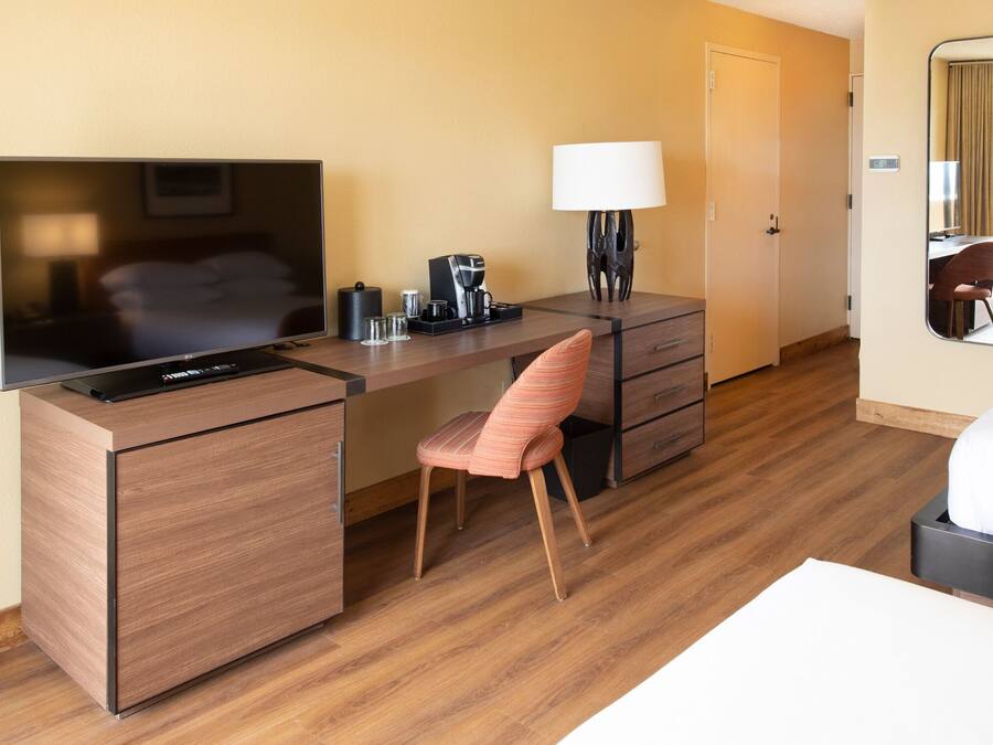 A hotel room with a wooden desk, a television, a lamp, a chair, and a bed.