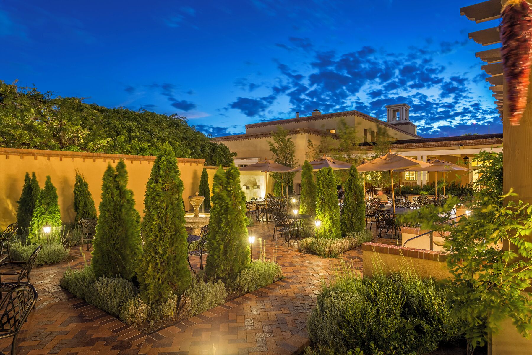 An outdoor patio area with tables and chairs, surrounded by greenery and a stone pathway.