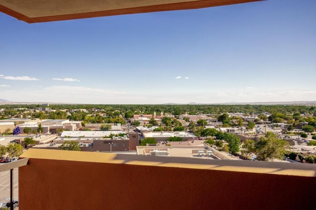 Un balcón con vistas a un paisaje urbano, que incluye edificios y zonas verdes.