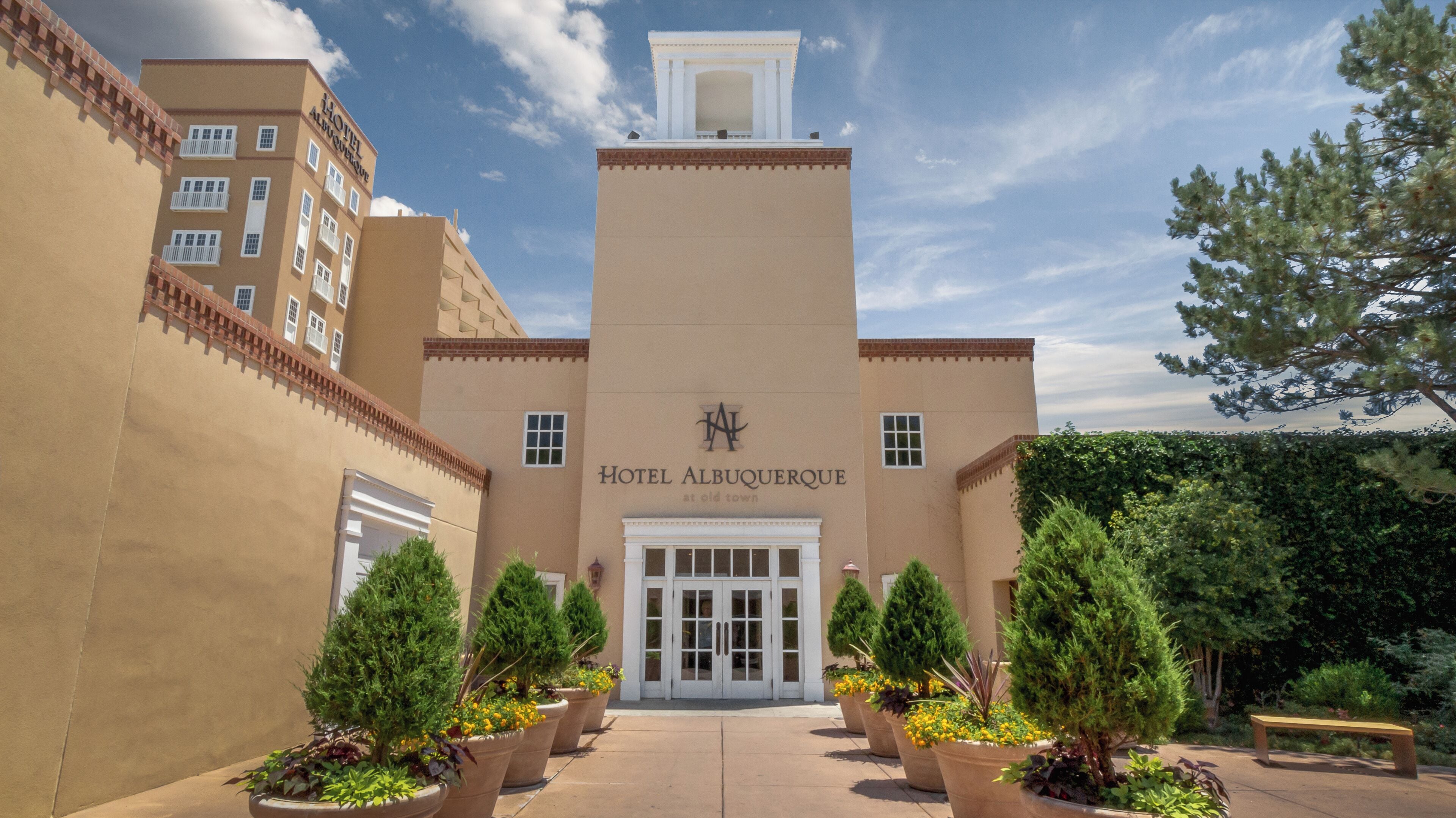 A hotel entrance with a central tower, potted plants, and a bench.