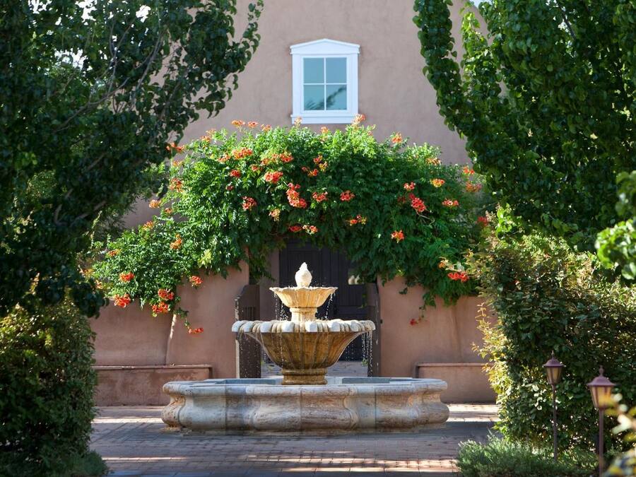 Une fontaine en pierre se trouve dans une cour, avec un bâtiment en arrière-plan.
